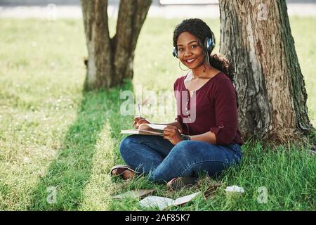 Si trova sull'erba. Allegro americano africano donna nel parco in estate Foto Stock