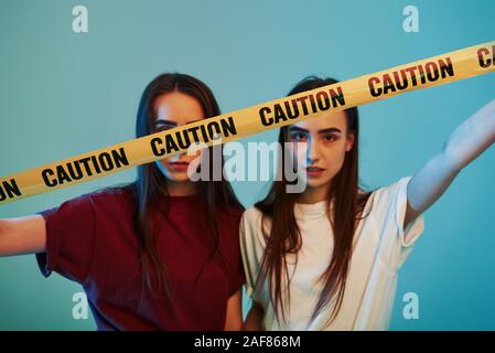 Dietro il giallo Nastro di avvertenza. Studio shot in interni con luce al neon. Foto di due bellissimi gemelli Foto Stock