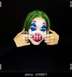 Ragazza con un trucco da clown ride follemente su sfondo scuro. Foto Stock
