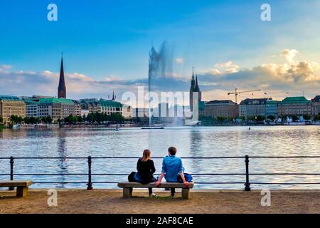 Coppia seduta su una panchina di fronte al Binnenalster (interno Lago Alster) al tramonto, Amburgo, Germania Foto Stock