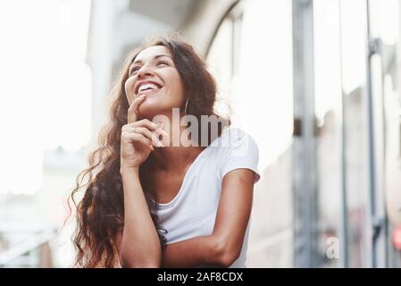 Guarda lontano e sorrisi. Bella donna con ricci capelli neri hanno un buon tempo nella città di giorno Foto Stock