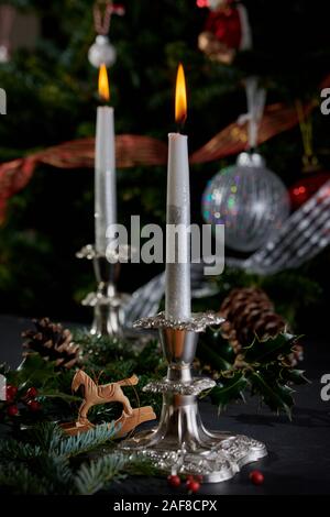 Flaming candele in argento antico portacandele con albero di Natale decorato a sfondo. Foto Stock