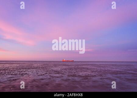 Un recipiente rosso passando la bocca del fiume Elb a bassa marea di fronte a un bel cielo color pastello a bassa marea del mare di Wadden vicino Otterndorf Foto Stock