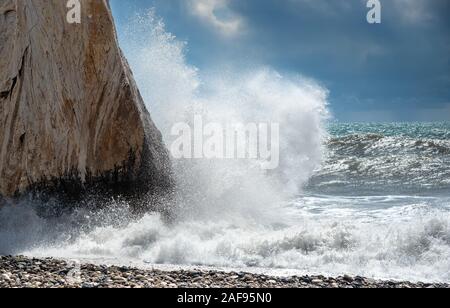 Spiaggia rocciosa con oceano ondulata e onde che si infrangono sugli scogli di roccia di Afrodite area di Paphos, Cipro Foto Stock