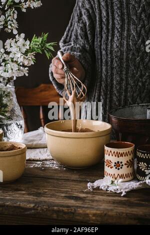 Una donna per la cottura di una torta di bundt a casa in una cucina rustica, su di un tavolo di legno. Foto Stock