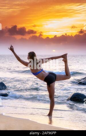 Una giovane donna di eseguire una posa yoga sulla spiaggia Foto Stock