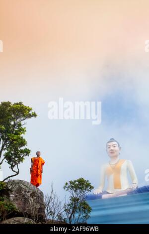 Un samanera o monaco novizio in piedi di fronte ad una gigantesca statua della divinità locale Yeay Mao, Bokor mountain, Kampot, Cambogia Foto Stock