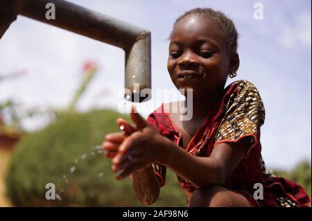 Allegro Piccolo African School Girl Drinks Cassaforte Acqua Potabile Fresca Pulita Da Home Tap Foto Stock