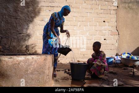 Silhouette ragazze africane la raccolta di acqua fresca da un rubinetto Foto Stock