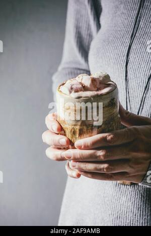 La donna in grigio maglione tenere in mani tazza ceramica con cioccolata calda o di cacao con marshmallow. Foto Stock