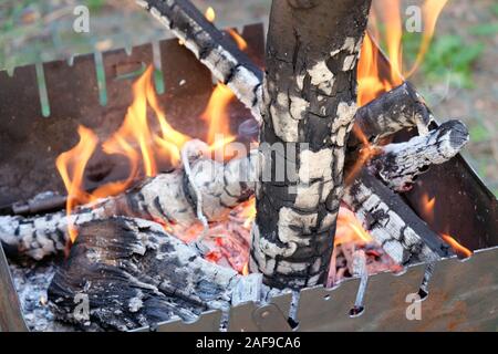 Metallo barbecue portatile sul terreno in cantiere. Il braciere è coperto di ruggine. La legna brucia in un barbecue, un arancio brillante fuoco. Un log in Foto Stock