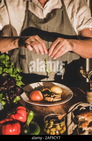 Eldery donna in lino grembiule mettendo le erbe toTurkish tradizionale zuppa di carne Haslama con verdure in cucina moderna con interni. Caduta comfort food, regio Foto Stock