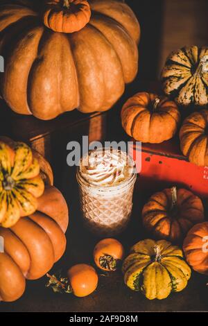 Pumpkin spice latte bevanda caffè conditi con panna montata in vetro tra freschi zucche e cachi. Autunno stagionali riscaldamento calda bevanda dolce Foto Stock