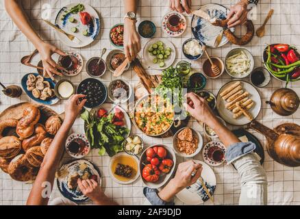 Flat-laici della Famiglia seduta a tavola con bagno turco colazione con dolci, verdure verdi, si diffonde, formaggi, uova, marmellate e tè in tulip bicchieri un Foto Stock