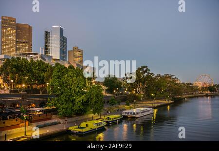 Melbourne, Australia - 17 Novembre 2009: il tramonto su dark Fiume Yarra con tre imbarcazioni fluviali. Alti grattacieli e ruota panoramica Ferris nel retro. Sera bl Foto Stock