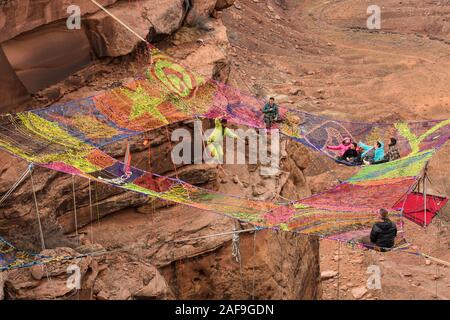 Un giovane uomo slacklining o highlining sullo Space Net a centinaia di metri di altezza sopra il Canyon minerali nei pressi di Moab Utah durante un raduno highline come il suo amico Foto Stock