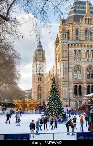Persone il pattinaggio su uno stadio del ghiaccio artificiale attorno a un albero di Natale al di fuori del Museo di Storia Naturale, Cromwell Road, Londra, Inghilterra Foto Stock