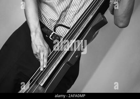 L'uomo gioca rosso moderno contrabbasso elettrico in studio musicale. Retrò stilizzata foto in bianco e nero Foto Stock