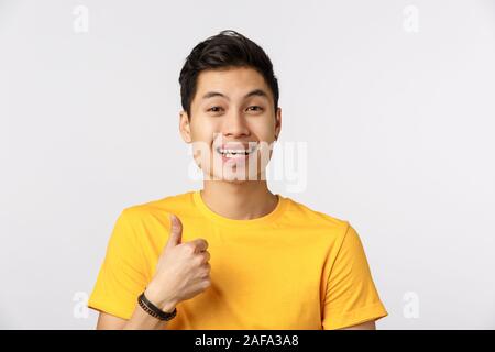 Close-up studio shot gioiosa, attraente maschio asiatici in giallo t-shirt, mostrando pollice in su e sorridente, come dare un feedback positivo, si consiglia di usare Foto Stock