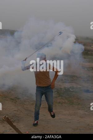 La striscia di Gaza. Xiii Dec, 2019. Un manifestante palestinese utilizza un slingshot a lanciare indietro una lacrima bombola del gas sparati dalle truppe israeliane durante scontri nella zona centrale della striscia di Gaza, Dic 13, 2019. Credito: Khaled Omar/Xinhua/Alamy Live News Foto Stock