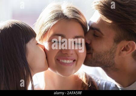 Piccola figlia e padre baciare sorridente madre moglie sulle guance Foto Stock