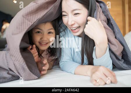 Madre e figlia bambino ragazza che gioca in camera da letto e mettere un lenzuolo sul . Felice famiglia asiatica Foto Stock