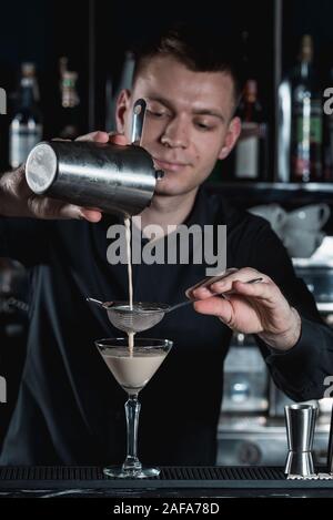 Barista facendo Espresso Martini cocktail, versando il liquido in vetro. Bar su uno sfondo Foto Stock