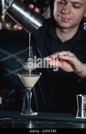 Barista facendo Espresso Martini cocktail, versando il liquido in vetro. Bar su uno sfondo Foto Stock