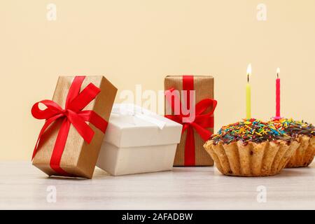 Confezioni regalo e gustosi compleanno muffin, decorata con la masterizzazione di festosa candele su legno e sfondo beige. Buon compleanno concetto. Foto Stock