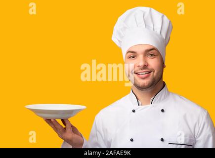 Lo Chef uomo piatto di servizio tenendo la piastra a vuoto su sfondo giallo Foto Stock