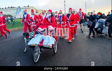 Brighton Regno Unito 14 Dicembre 2019 - centinaia tra cui bambini e cani prendere parte al Brighton Santa Dash in una giornata di vento lungo il lungomare aiutando a raccogliere fondi per la Rockinghorse la carità che è il braccio di raccolta fondi della Royal Alexandra ospedale per bambini . Credito: Simon Dack / Alamy Live News Foto Stock