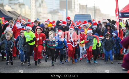 Brighton Regno Unito 14 Dicembre 2019 - centinaia tra cui bambini e cani prendere parte al Brighton Santa Dash in una giornata di vento lungo il lungomare aiutando a raccogliere fondi per la Rockinghorse la carità che è il braccio di raccolta fondi della Royal Alexandra ospedale per bambini . Credito: Simon Dack / Alamy Live News Foto Stock