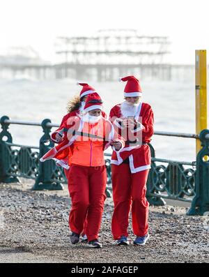 Brighton Regno Unito 14 Dicembre 2019 - centinaia tra cui bambini e cani prendere parte al Brighton Santa Dash in una giornata di vento lungo il lungomare aiutando a raccogliere fondi per la Rockinghorse la carità che è il braccio di raccolta fondi della Royal Alexandra ospedale per bambini . Credito: Simon Dack / Alamy Live News Foto Stock