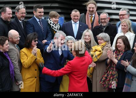 Primo Ministro Nicola Storione abbracci SNP Westminster leader Ian Blackford (seconda a sinistra) come lei si unisce SNP neoeletto MPs per una foto di gruppo chiamata al di fuori del V&un museo di Dundee. Foto Stock