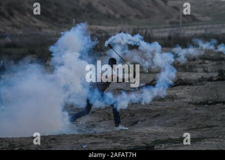 Dicembre 13, 2019: Gaza, Palestina. Il 13 dicembre 2019. Dimostranti palestinesi scontro con le forze israeliane ad est del Bereij al campo di rifugiati nella zona centrale della striscia di Gaza, durante questo venerdì una Grande Marcia di protesta di ritorno. I dimostranti avevano raccolto lungo il confine, con alcuni che lanciano pietre verso i soldati israeliani di stanza sull'altro lato della recinzione di separazione. Le forze israeliane hanno sparato gas lacrimogeni e proiettili a manifestanti, ferendo un certo numero di essi. Il grande marzo di restituire le proteste hanno avuto inizio presso la frontiera Gaza il 30 marzo 2018 a chiamata per il sollevamento del blocco israeliano su Foto Stock