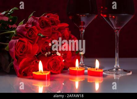 Bouquet di rose rosse e due bicchieri di vino con candele accese su un bianco riflettente piano portapaziente Foto Stock