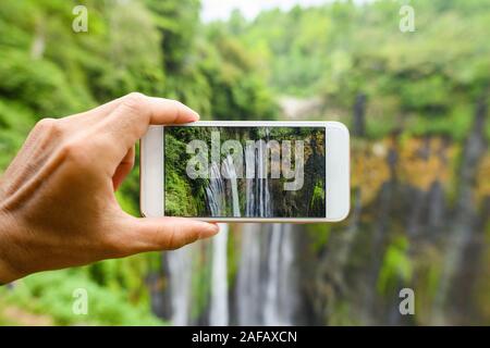 Un turista è di scattare foto con uno smartphone per la bella Tumpak Sewu cascate. Tumpak Sewu cascate sono un'attrazione turistica in Giava Est. Foto Stock