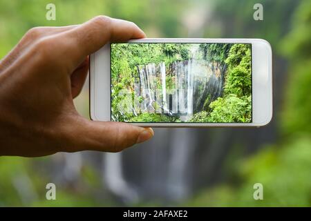 Un turista è di scattare foto con uno smartphone per la bella Tumpak Sewu cascate. Tumpak Sewu cascate sono un'attrazione turistica in Giava Est. Foto Stock