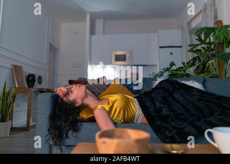 Malato e malato giovane donna recante sul divano di casa con la temperatura al di sotto di una coperta. Donna sorpresa influenza e freddo. Emicrania e mal di testa Foto Stock