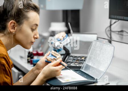 Donna tecnico colorazione protesi dentale con una spazzola di vernice presso il laboratorio. Concetto di produzione implantats Foto Stock