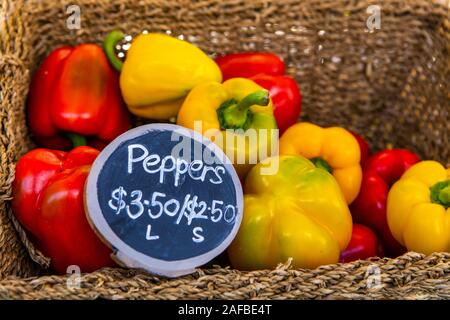 Una vista ravvicinata di un rustico cesto in vimini riempito con organici peperoni, Capsicum, con un cartellino del prezzo su un mercato in stallo alla fiera locale per gli agricoltori Foto Stock