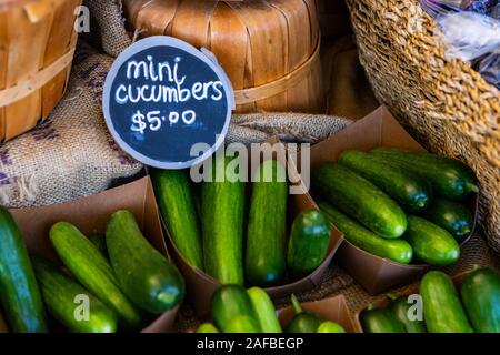 Un angolo alto e immagine ravvicinata di biologico mini cetrioli visualizzati in piccole scatole su un mercato in stallo durante un locale raccolto agricolo fiera. Foto Stock