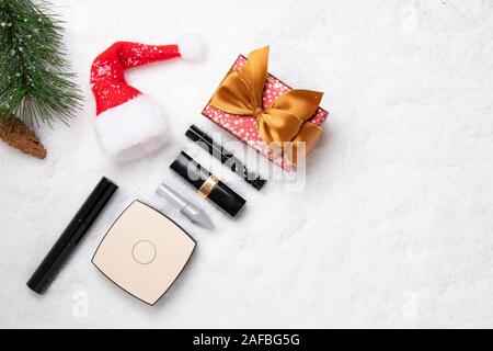 Natale sfondo dei cosmetici. Vista dall'alto su vari prodotti cosmetici e accessori bellezza, un dono, un cappello da Babbo Natale e un ramo di abete bianco sulla neve. Spa Foto Stock