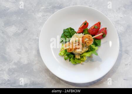 Antipasto di spiedini di gamberi su un risotto cavolfiore heap, lattuga e pomodoro su una piastra bianca, sfondo grigio chiaro con copia spazio, alta angelo Foto Stock