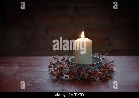 Candela che brucia in una ciotola con una corona piccola dalla rosa canina e argento cuscino sulla boccola in rosso di un tavolo di legno, decorazione invernale per l Avvento e Natale Foto Stock