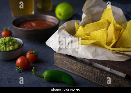 Fotografia di cibo di una scatola con nachos o tortilla chips con salsa guacamole e dip e di birra messicana o cerveza Foto Stock