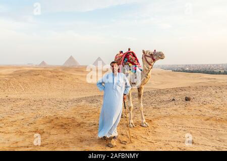 Africa, Egitto, al Cairo. Altopiano di Giza. Il 3 ottobre 2018. Driver di cammello con cammello vicino alle piramidi di Giza. Foto Stock