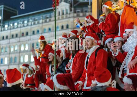 Trafalgar Square, Londra, Regno Unito. 14 dicembre 2019. Una grande folla vestita con costumi di Babbo Natale si riunisce a Trafalgar Square, Londra, durante il SantaCon 2019. La scena notturna cattura le festività natalizie, con i partecipanti che sorridono, tengono bevande e si impegnano in festeggiamenti a tema natalizio. Lo sfondo presenta l'architettura classica del centro di Londra, illuminata dall'illuminazione urbana. L'immagine riflette la gioia comune, lo spirito stagionale e la tradizione giocosa in uno spazio civico pubblico. Penelope Barritt/Alamy Live News Foto Stock