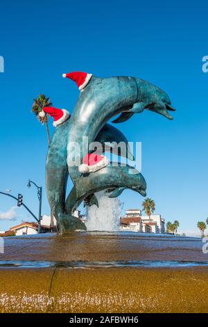 Scultura di tre delfini in bronzo che indossa il bianco e il rosso cappelli di Babbo Natale per la stagione di Natale all'entrata di Stearn's Wharf a Santa Barbara, CA. Foto Stock