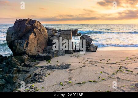 Mare spiaggia a sunrise. onde calme lavare le rocce enormi. golden nuvole sul cielo. incredibile paesaggio marino nella luce del mattino. Foto Stock